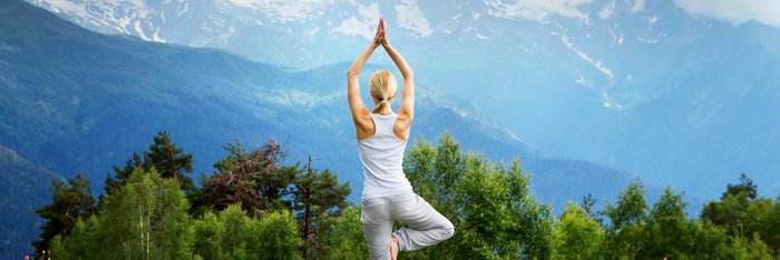 Eine blonde Frau übt Yoga auf einer Weide in den Bergen
