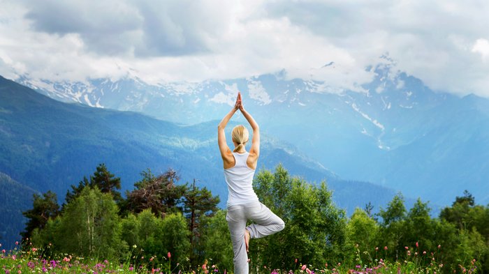 Eine blonde Frau übt Yoga auf einer Weide in den Bergen