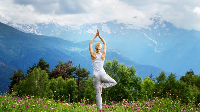 Eine blonde Frau übt Yoga auf einer Weide in den Bergen