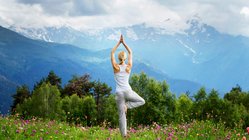Eine blonde Frau übt Yoga auf einer Weide in den Bergen