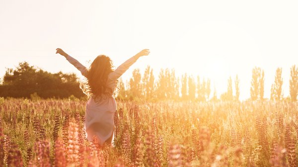 Glückliche Frau in grüner Blumenwiese hebt die Hände zum Himmel