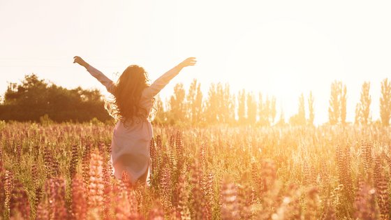 Glückliche Frau in grüner Blumenwiese hebt die Hände zum Himmel