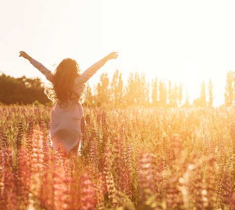Glückliche Frau in grüner Blumenwiese hebt die Hände zum Himmel