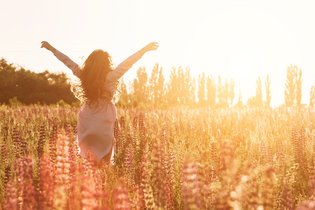 Glückliche Frau in grüner Blumenwiese hebt die Hände zum Himmel